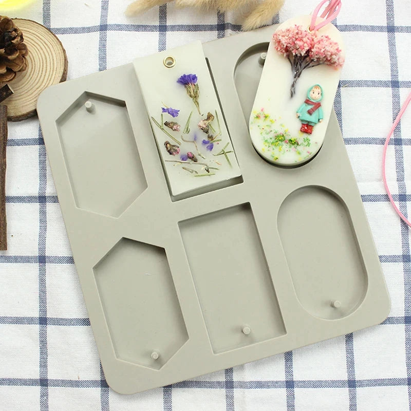 A gray silicone mold tray holds a pink floral soap bar and a small green figurine.