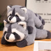 A pair of gray and white raccoon plush toys lying on a wooden surface.