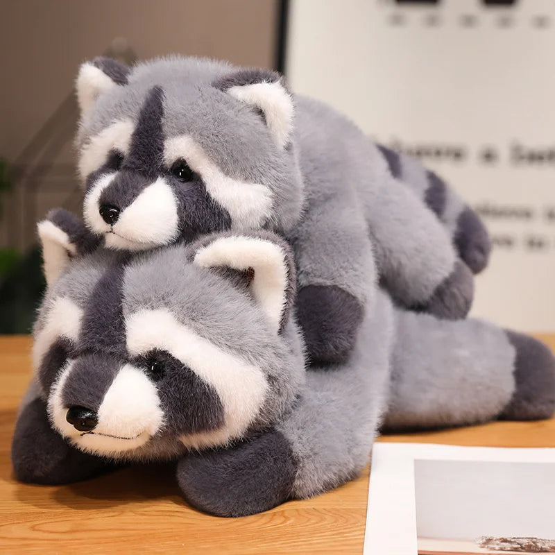A pair of gray and white raccoon plush toys lying on a wooden surface.