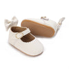 A pair of white lace-trimmed baby girl moccasin shoes with a bow and tan leather lining.