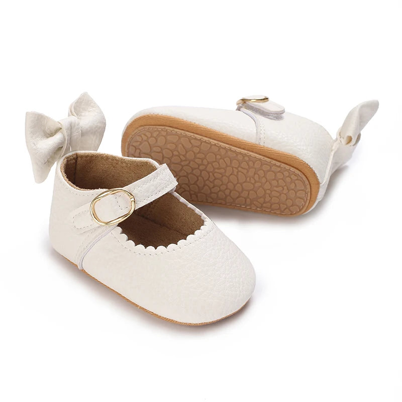 A pair of white lace-trimmed baby girl moccasin shoes with a bow and tan leather lining.