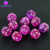 A collection of ten glitter polyhedral dice in various shades of purple and pink resting on a dark surface.