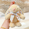 A fluffy light brown bunny plush toy with a pink nose and a floral bow charm being held by a hand.