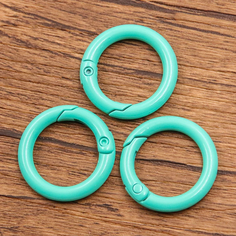 Four bright turquoise metal O-ring spring clasps arranged in a cluster on a wooden surface.