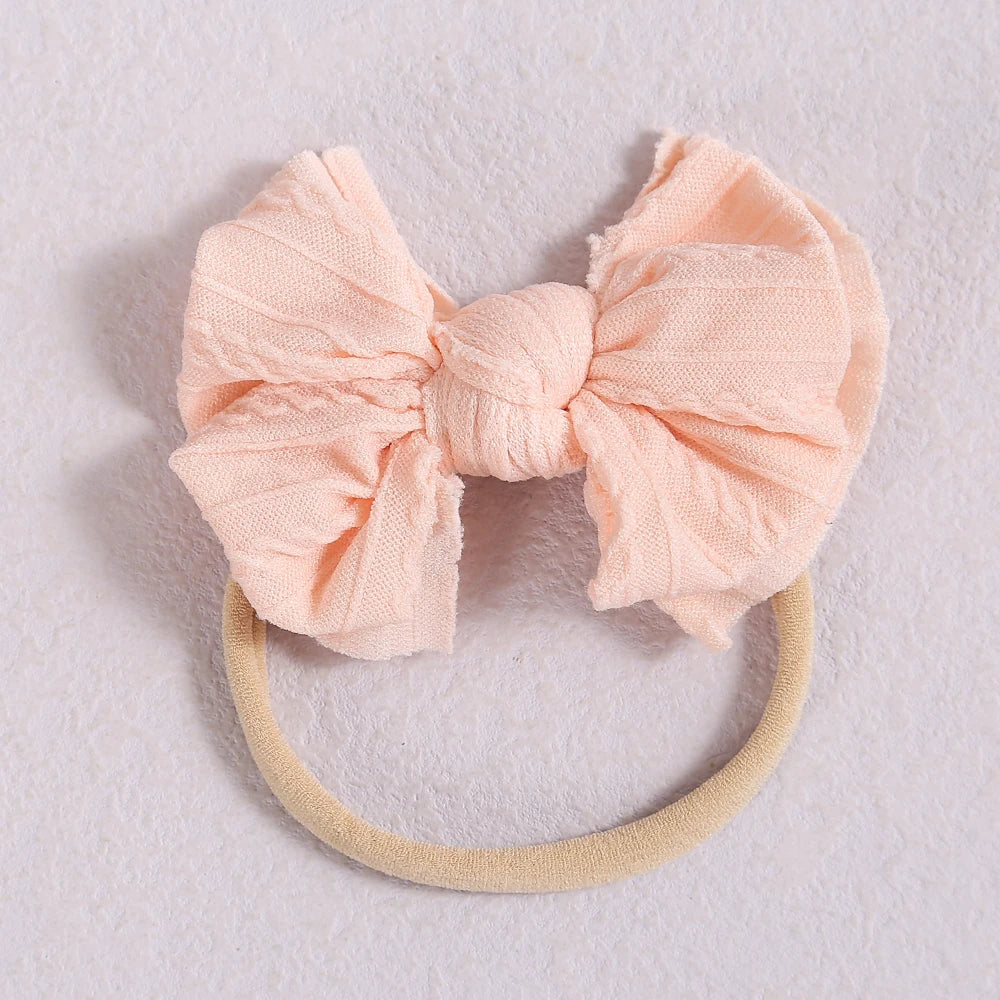 A soft peach pink fabric bow headband with a light beige elastic band.