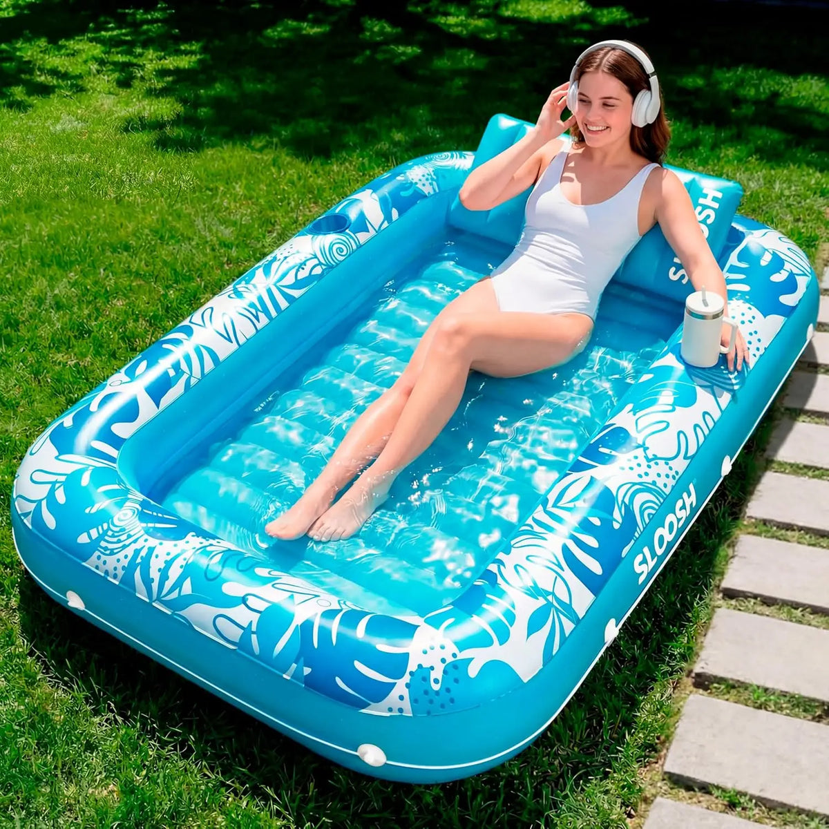 A woman relaxing in a blue inflatable float on the grass with headphones.