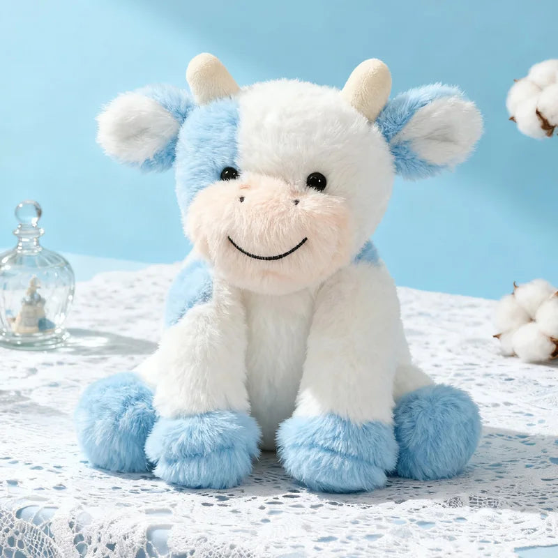 A fluffy white and blue sitting cow plush toy with soft fur resting on a white lace surface.