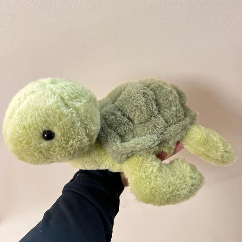A hand is holding a soft, light green simulated turtle plush doll.