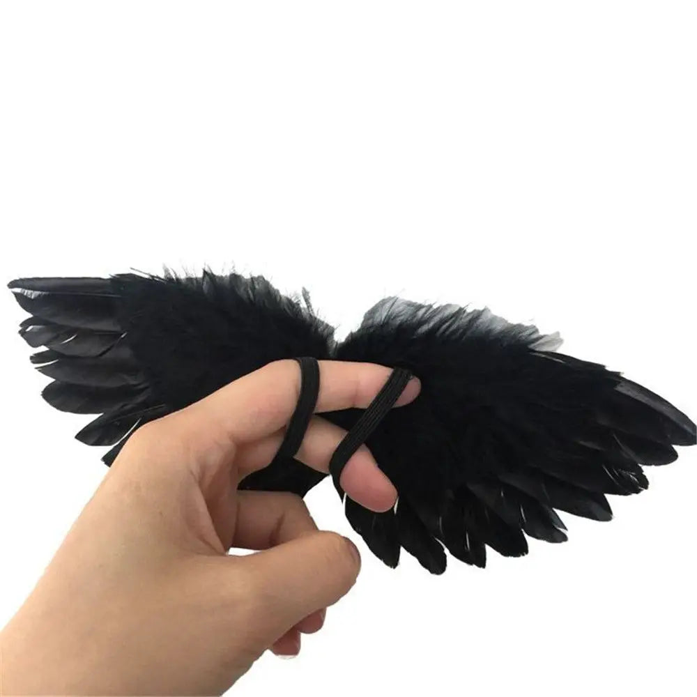 A hand holds a pair of black mini feather angel wings for dolls and crafts.