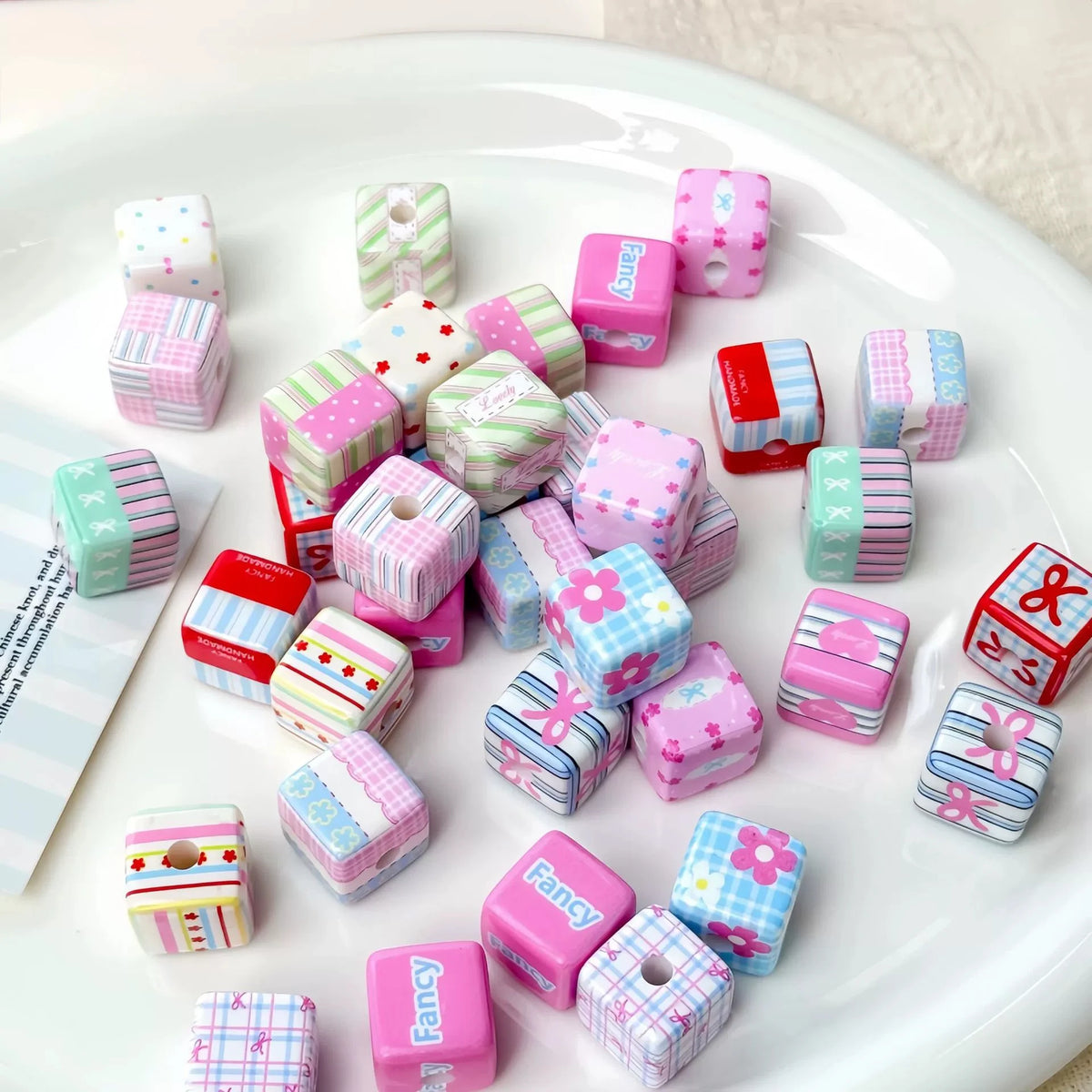 A variety of pink, green, and white acrylic flower print beads and bow charms are displayed on a white plate.