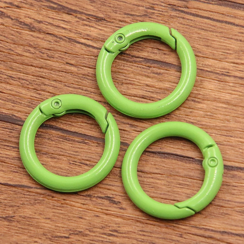 A set of ten bright lime green metal O-ring spring clasps arranged on a wooden surface.