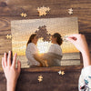 Hands are assembling a custom photo puzzle featuring two people against an sunset background.
