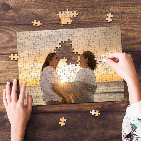 Hands are assembling a custom photo puzzle featuring two people against an sunset background.