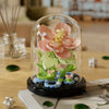 A clear glass dome showcases a miniature buildable eternal rose flower kit featuring pink and green floral elements.