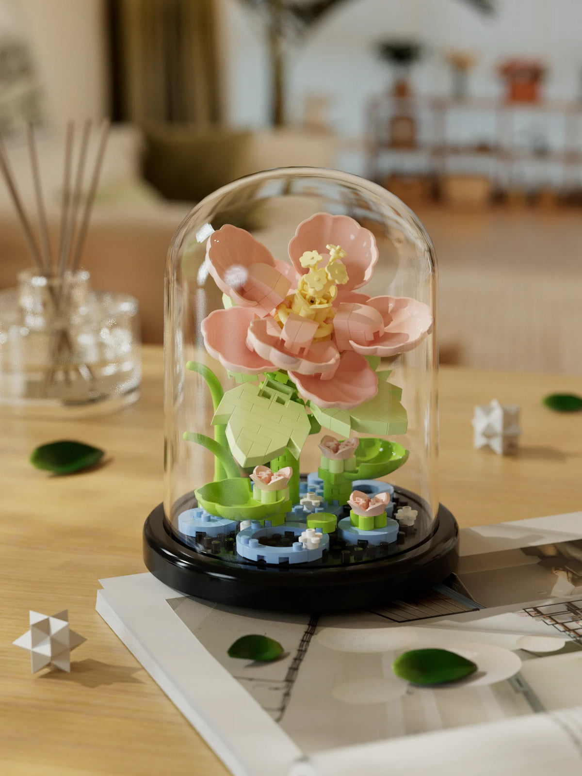 A clear glass dome showcases a miniature buildable eternal rose flower kit featuring pink and green floral elements.