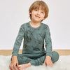 A young boy wearing a long-sleeved, long pants cotton pajama set with an astronaut print, sitting on a white rug.
