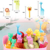 A set of kawaii mini fruit forks in various colors and shapes, including a giraffe, lion, and cat, displayed on a pink plate 