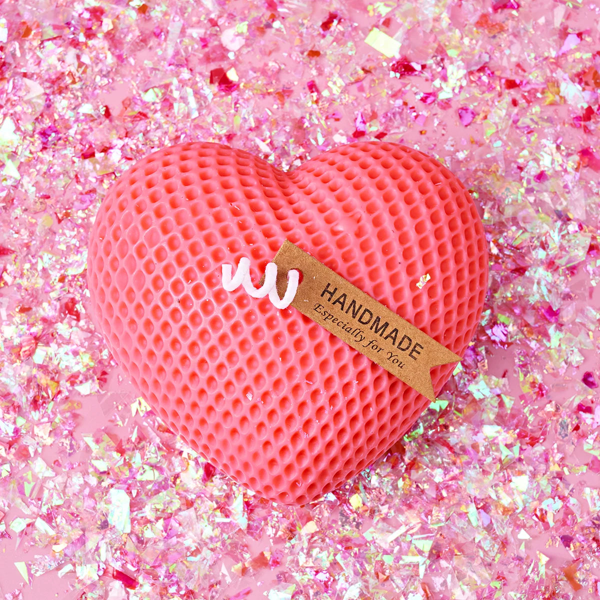 A pink heart-shaped silicone mold with a honeycomb texture is displayed on a bed of pink glitter.