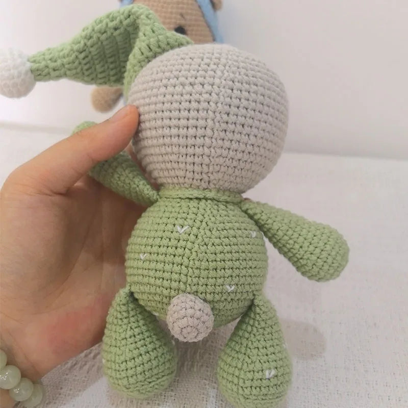 A hand holds a handmade crochet stuffed bear toy in light green color.