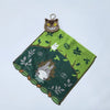 A green embroidered fabric featuring a small brown cat plush toy on a white background.
