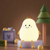A white pear-shaped night light with yellow accents sits on a wooden surface.