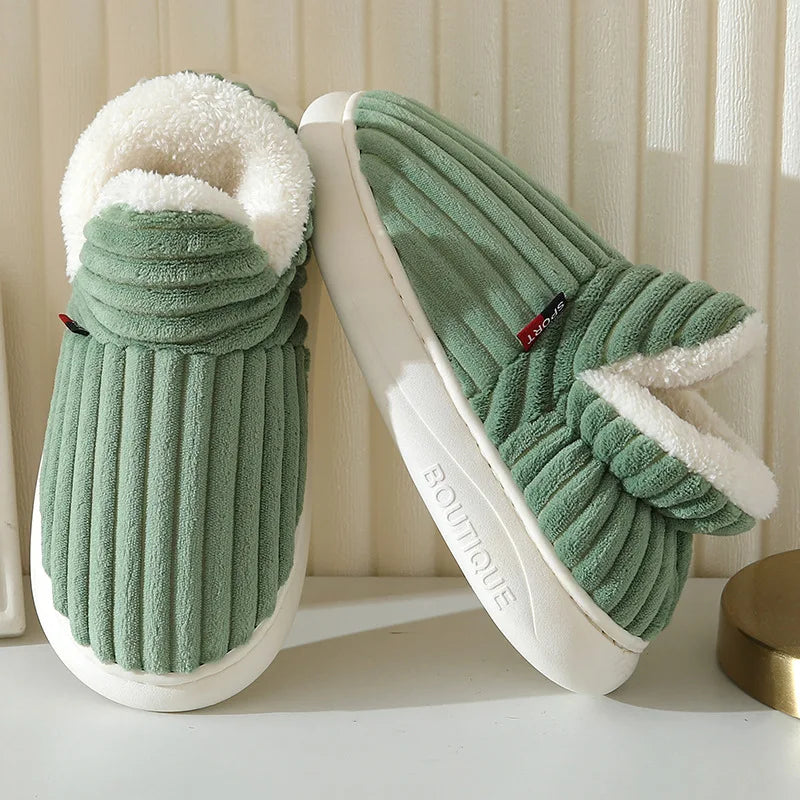 A pair of olive green faux fur slippers with white soles and light green ribbed fabric are shown on a white surface.