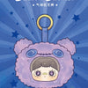 A plush blind box featuring a face with large eyes and a fluffy purple body, suspended by a gold bag clip.