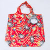 A red fabric bag featuring a pattern of white and yellow floral designs with a gray hippo plush toy attached.