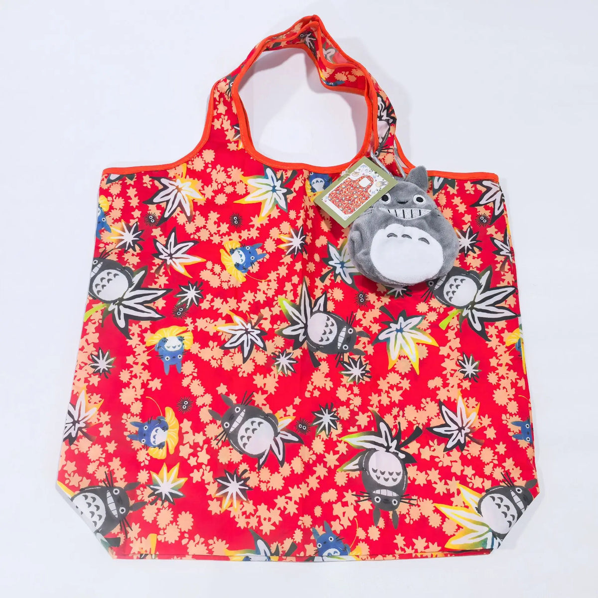 A red fabric bag featuring a pattern of white and yellow floral designs with a gray hippo plush toy attached.