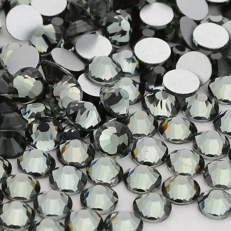 A close-up view of various clear and dark glass crystal flatback rhinestones for nail art and crafts.
