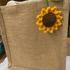 Handmade crochet sunflower charm attached to a beige woven fabric pouch.
