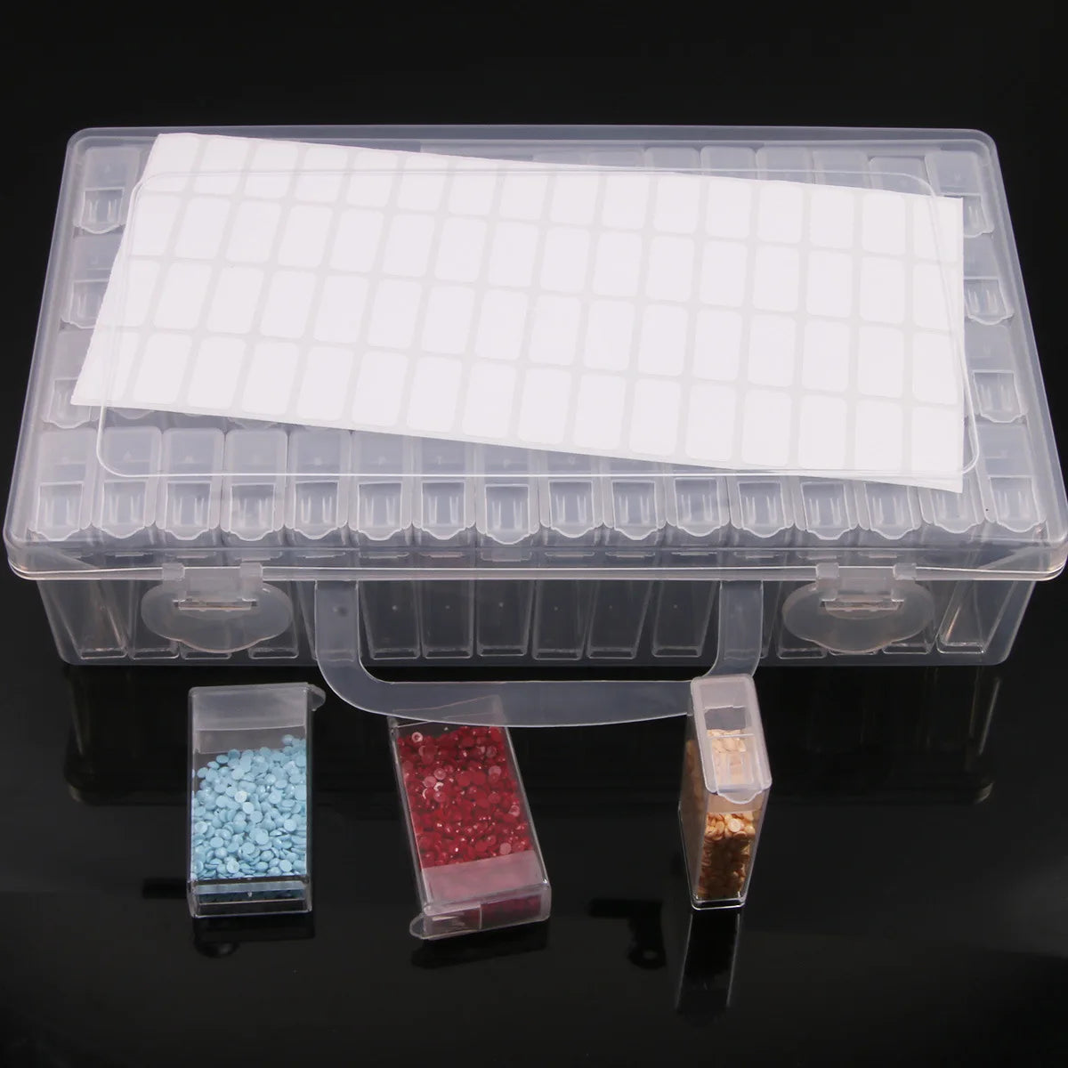 A clear plastic storage box for diamond painting supplies featuring an organizer tray and small compartments for beads or gem