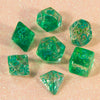 A collection of green glitter polyhedral dice, including D4, D6, D8, D10, D00, D12, and D20, scattered on a pink surface.