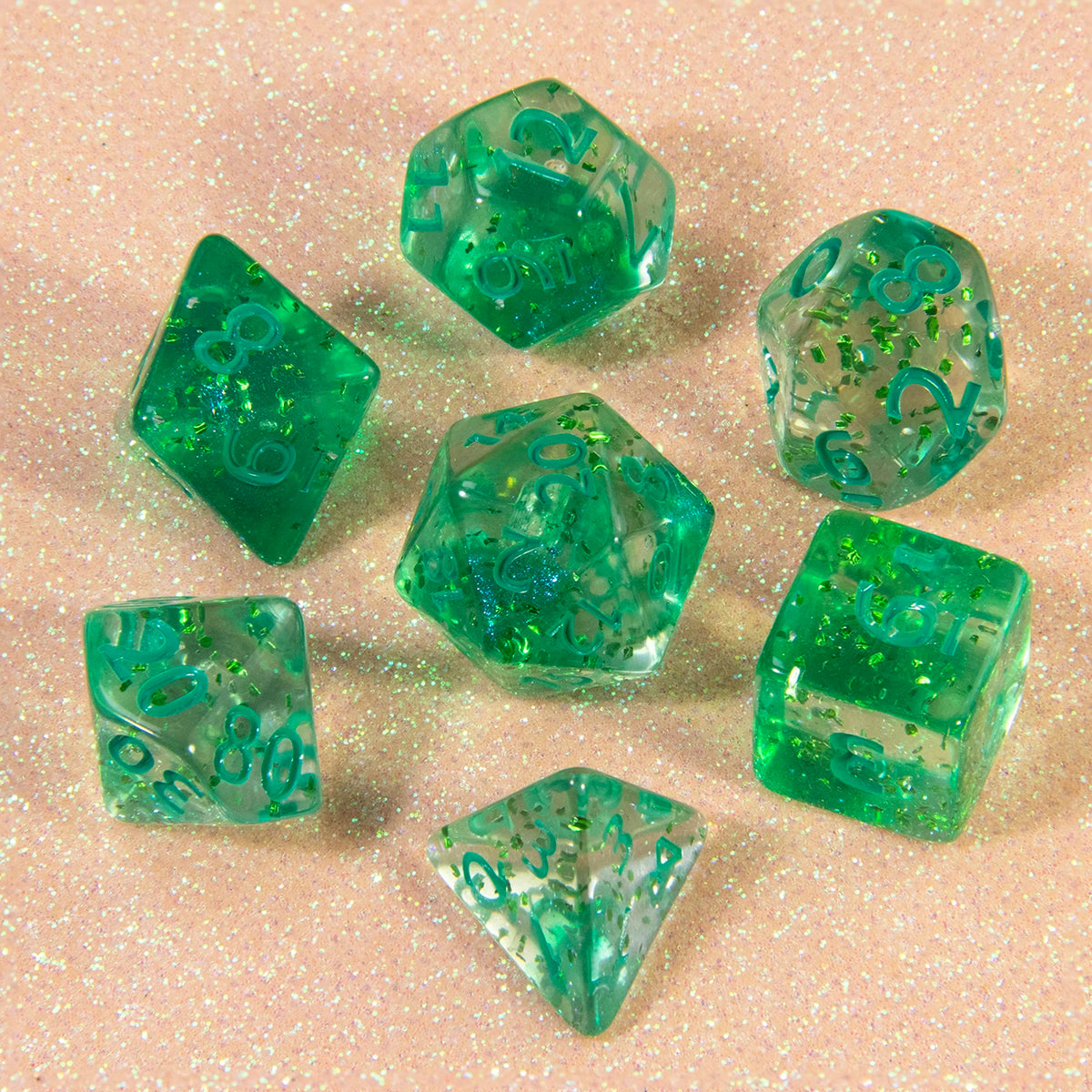 A collection of green glitter polyhedral dice, including D4, D6, D8, D10, D00, D12, and D20, scattered on a pink surface.