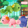 A beginner crochet kit for amigurumi animals showing a green frog and a pink hedgehog among yarn and tools.