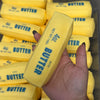 A hand holds a yellow butter stick squishy stress ball with the label 4oz butter salted.