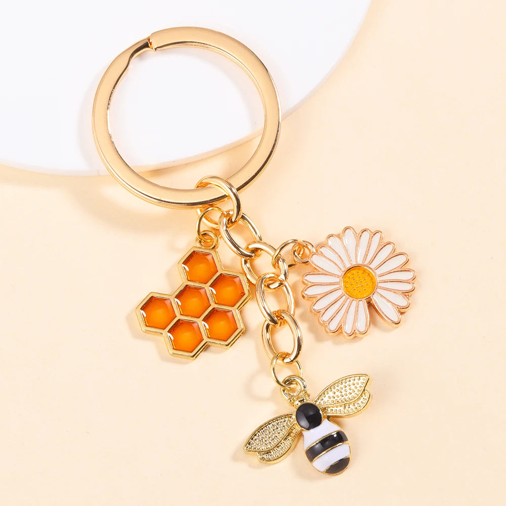 Gold-toned keychain featuring an enamel flower and a bee charm on a light beige background.
