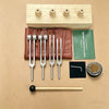 A set of calibrated sound healing tuning forks and a wooden resonance box are displayed on a beige background.