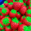 A pile of bright red strawberry stress balls with green leaves.