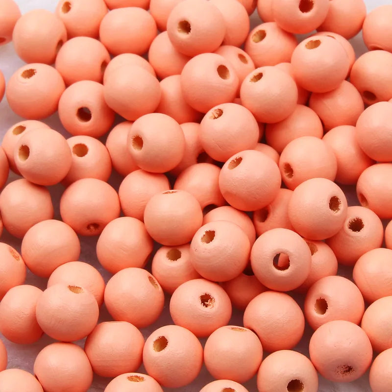 A pile of small, round, natural wooden beads in a light coral or peach color.