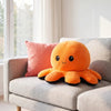 An orange flip octopus plush toy resting on a light gray sofa.