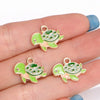 Two enamel marine life charms shaped like turtles in green and peach colors are displayed on a hand.