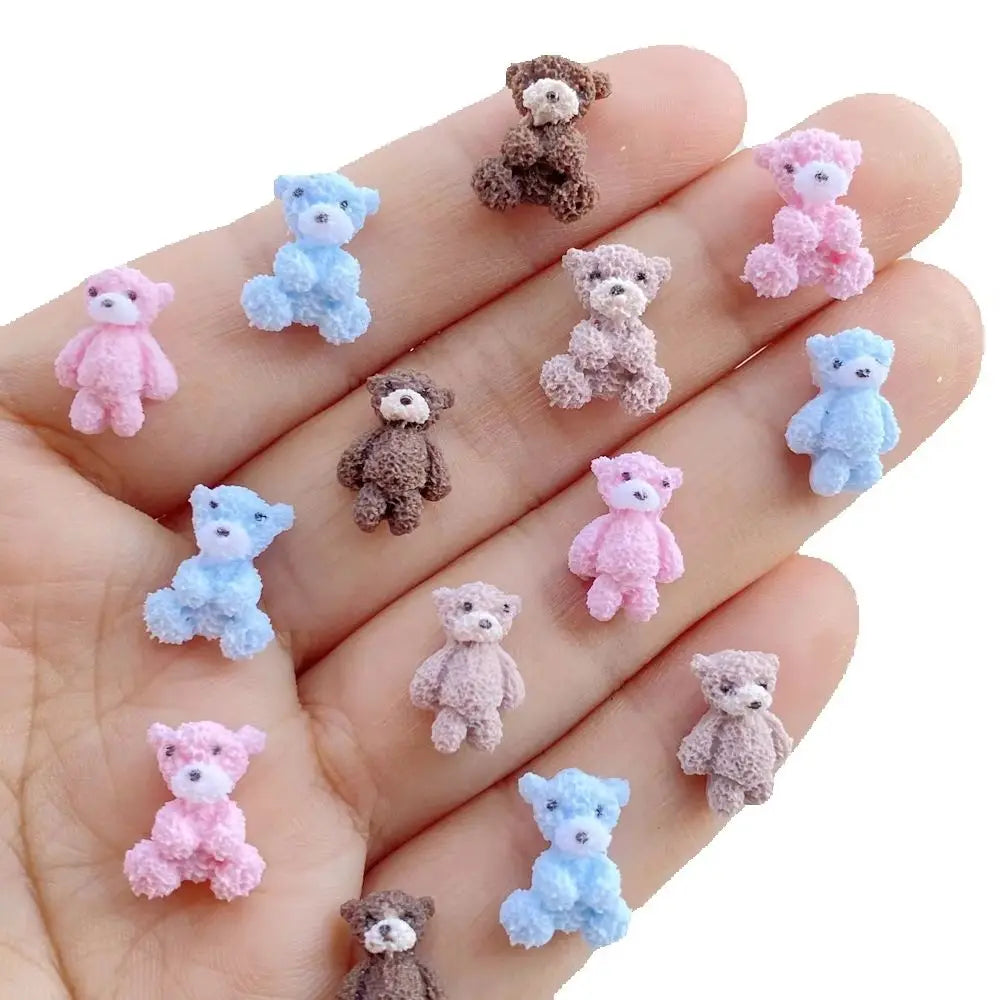 A hand displays various mini resin teddy bear charms in pink, blue, and brown colors.
