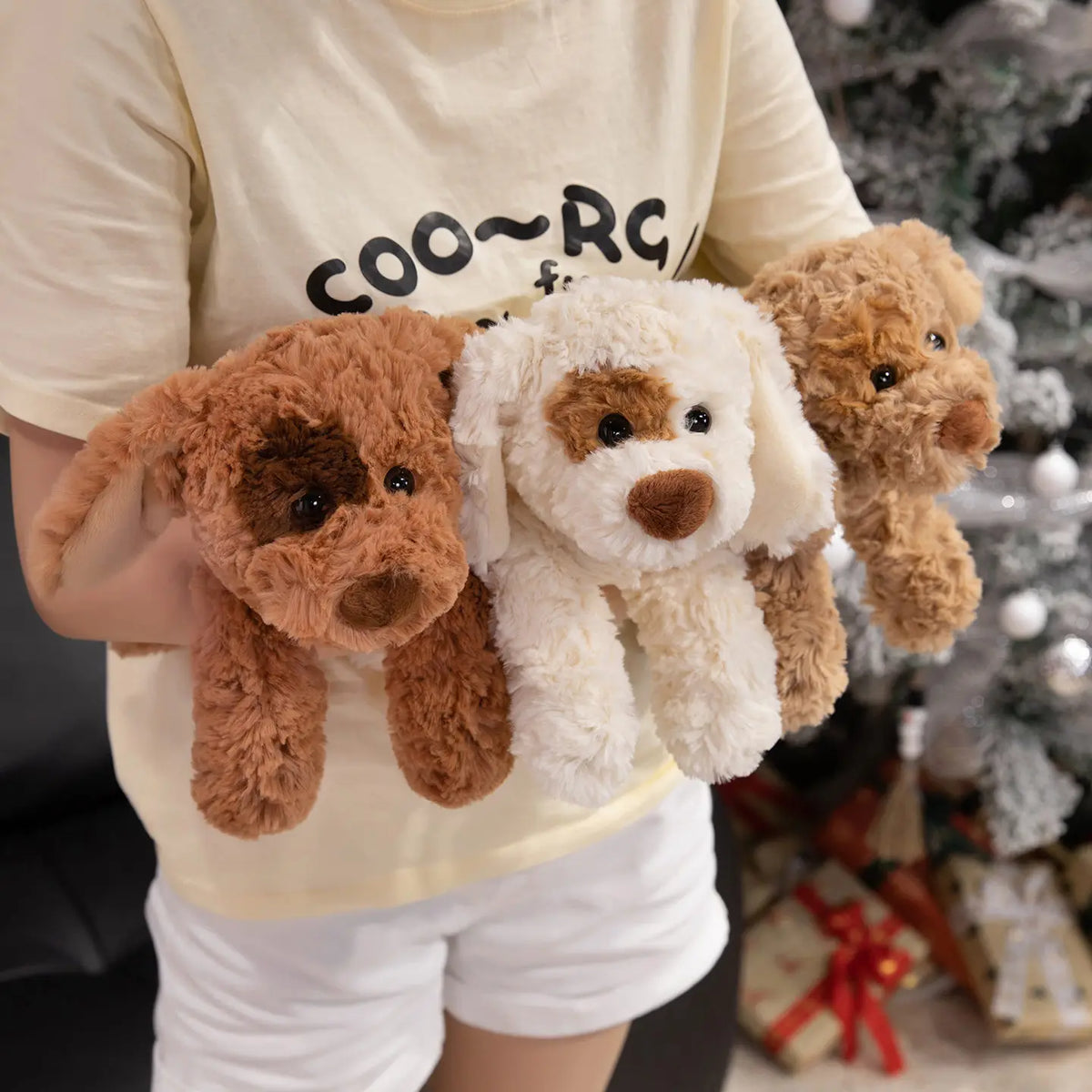 Una persona sostiene un peluche de perro marrón y un peluche de perro blanco.