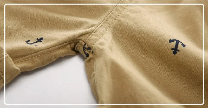 Close-up of tan cotton beach shorts featuring small navy blue anchor prints on the fabric.