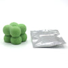 A pile of green candle dye chips for wax, next to a small plastic bag labeled GREEN.