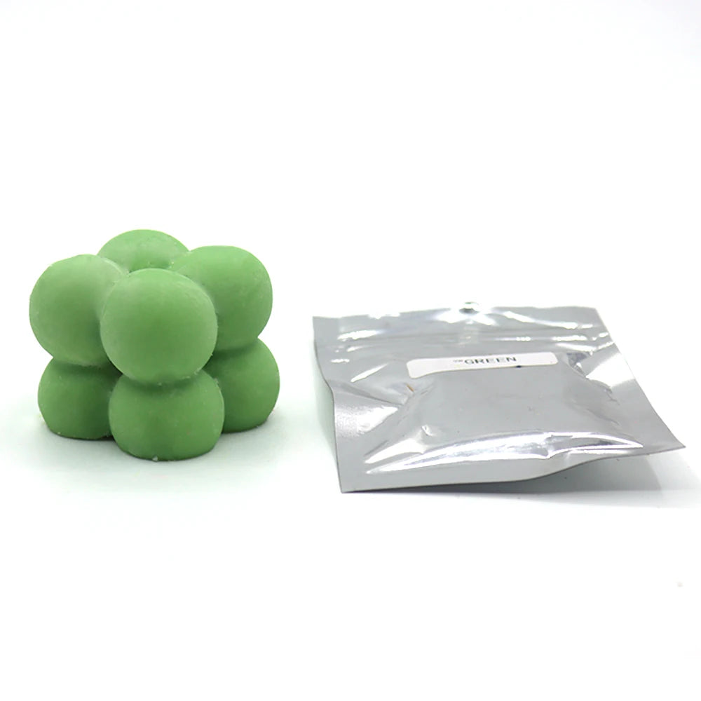 A pile of green candle dye chips for wax, next to a small plastic bag labeled GREEN.