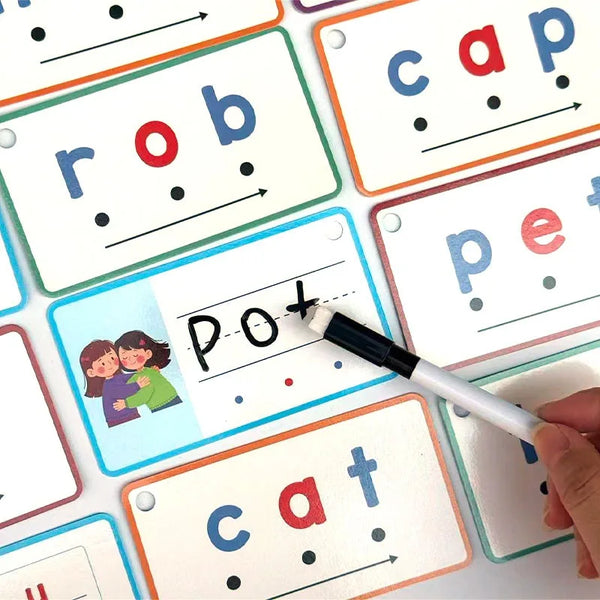 A hand holds a black pen writing on a flashcard with the word POT and dots, surrounded by other CVC word recognition cards.
