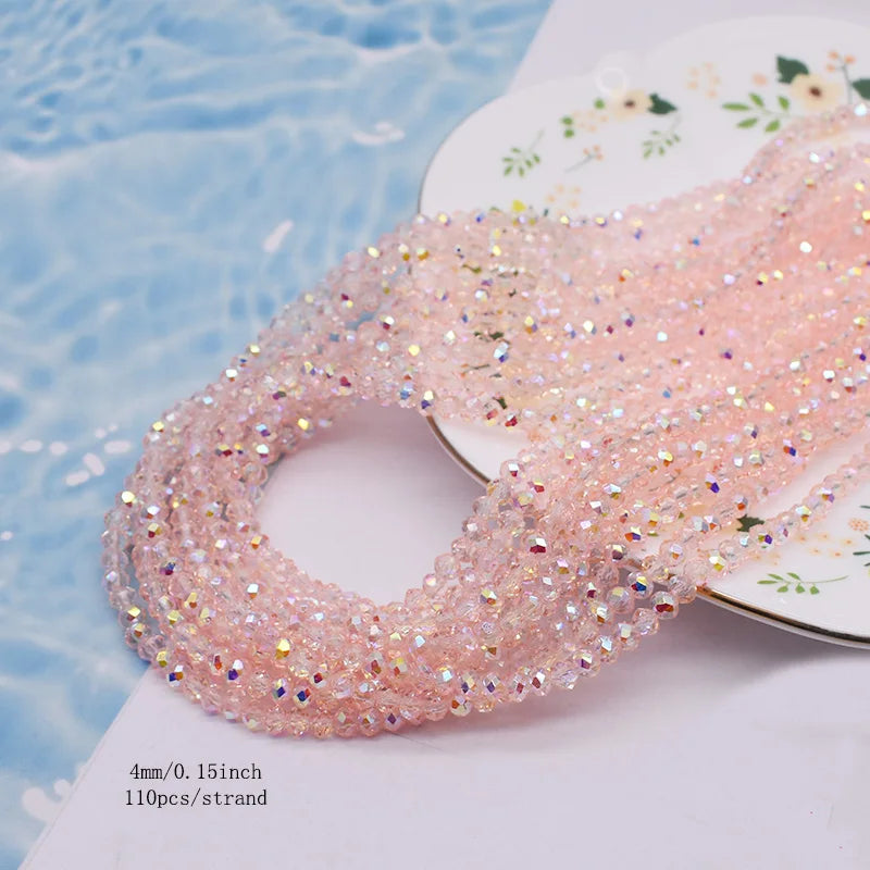 Pink faceted crystal rondelle beads for jewelry making displayed on a white surface next to blue water.