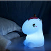 A white unicorn LED night light with a pink horn and touch control resting on a dark surface.